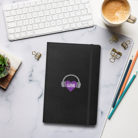 Image of A black "Boss Uncaged: Unleashing Ideas - I Love Podcasting" Hardcover Notebook with headphones on it next to a keyboard and a cup of coffee.