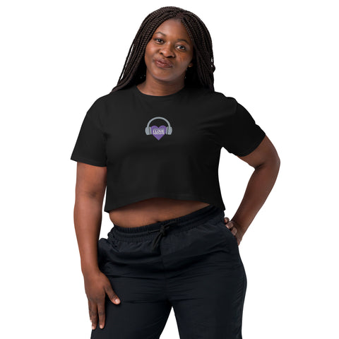 A woman donning a trendy black Affirmation I Love Podcasts - Women’s crop top from the Boss Uncaged Store and stylish purple headphones, engrossed in her favorite podcast "Boss Uncaged.