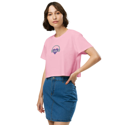 A woman wearing the Boss Uncaged Store Affirmation I Love Podcasts women's crop top, which is pink and features a purple heart, radiating an affirmation of love for podcasts.