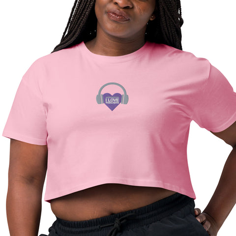 A woman wearing a pink Affirmation I Love Podcasts - Women's Crop Top from Boss Uncaged Store with headphones on it.