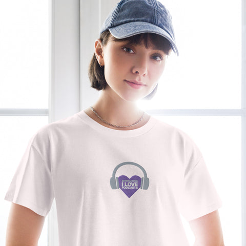 A woman wearing a white t-shirt with headphones and a purple heart, embodying the essence of Boss Uncaged Store's Affirmation I Love Podcasts - Women’s crop top and affirming her love for podcasts.