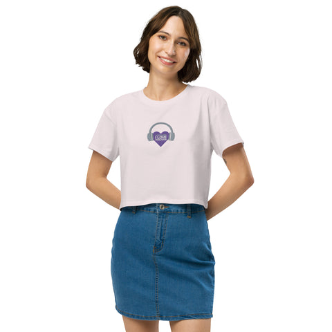 A woman wearing a Boss Uncaged Store Affirmation I Love Podcasts women's crop top with a purple heart on it, while listening to podcasts.
