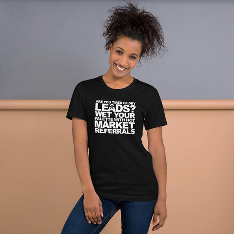 Image of A person is standing against a two-tone wall, smiling and wearing a black t-shirt from Buteke that features humorous white text stating "ARE YOU TIRED OF DRY LEADS? WET YOUR PALETTE WITH HOT MARKET REFERRALS," showcasing the power of networking.