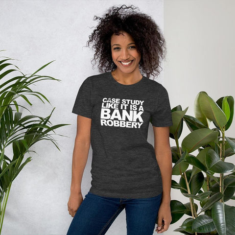 Image of A person with curly hair is smiling and wearing a dark gray Buteke T-shirt with the text "CASE THE STUDY LIKE IT IS A BANK ROBBERY! GIMME THE LOOT!" printed on it. There are green plants beside them, bringing your products to life and enhancing customer perception.