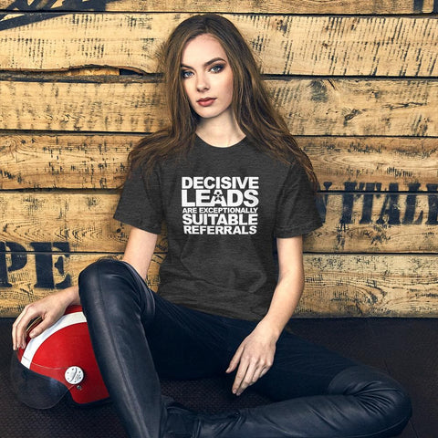 Image of A young woman with long hair sits on the floor, leaning against a wooden backdrop. She wears a dark gray T-shirt by Buteke that features the phrase "DECISIVE LEADS ARE AN EXCEPTIONALLY SUITABLE REFERRAL" and black pants.