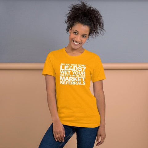 Image of A woman with curly hair, wearing a yellow Buteke T-shirt featuring white text that reads, "ARE YOU TIRED OF DRY LEADS? WET YOUR PALETTE WITH HOT MARKET REFERRALS.", stands in front of a gray and beige wall, smiling. The T-shirt is perfect for those diving into networking.