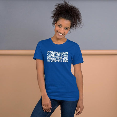 Image of A person with curly hair, wearing a blue Buteke t-shirt featuring the white text "COMPELLING CASE STUDIES ARE BYPRODUCTS OF CONSTRUCTED STORYTELLING," is standing against a two-tone wall.