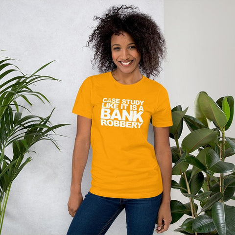 Image of A person stands in front of a light-colored wall and plants, wearing a yellow T-shirt from Buteke with the text "CASE THE STUDY LIKE IT IS A BANK ROBBERY! GIMME THE LOOT!,” ready to bring your products to life.