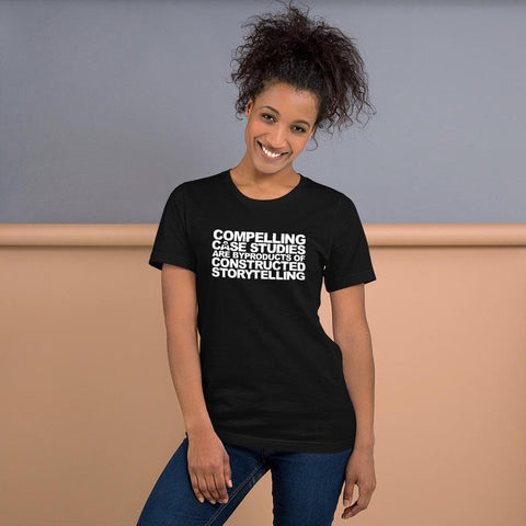 Image of A woman with curly hair smiles while wearing a black t-shirt from Buteke. The shirt has white text that reads, "Compelling Case Studies Are Byproducts of Constructed Storytelling.