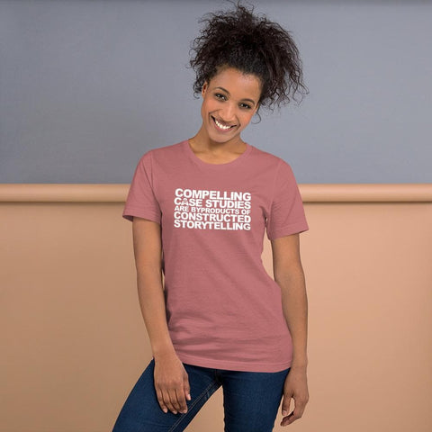 Image of A person with curly hair smiles while wearing a pink Buteke t-shirt featuring white text that reads, “COMPELLING CASE STUDIES ARE BYPRODUCTS OF CONSTRUCTED STORYTELLING.”