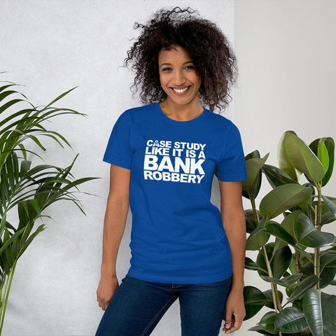 Image of A person with curly hair, wearing a blue t-shirt by Buteke that reads "CASE THE STUDY LIKE IT IS A BANK ROBBERY! GIMME THE LOOT!," stands smiling beside potted plants, bringing your products to life.