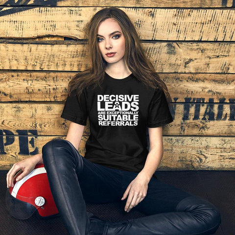 Image of A woman with long hair, dressed in a black Buteke t-shirt that reads “DECISIVE LEADS ARE AN EXCEPTIONALLY SUITABLE REFERRAL,” sits on the ground near a red and white helmet against a wooden backdrop, exuding confidence from her understanding of the power of effective leads.