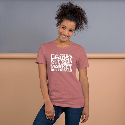 Image of A woman wearing a Buteke pink t-shirt with the text "ARE YOU TIRED OF DRY LEADS? WET YOUR PALETTE WITH HOT MARKET REFERRALS." stands in front of a gray and peach wall, embodying the power of effective networking.