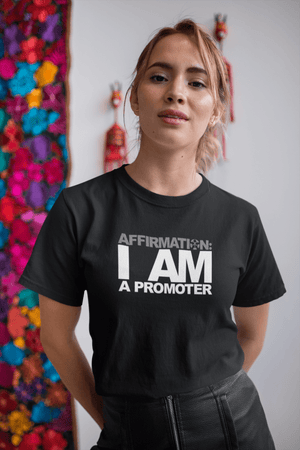 A woman wearing a black t-shirt that says AFFIRMATION: “I AM A PROMOTER” from the Boss Uncaged Store.