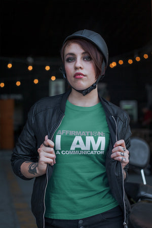 A woman wearing a green t-shirt that says "AFFIRMATION: I AM A COMMUNICATOR" from Boss Uncaged Store.