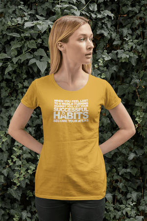 A woman wearing a yellow t-shirt with the words "WHEN YOU FEEL LOST TO A WORLD TURNING AGAINST YOU, LET YOUR SUCCESSFUL HABITS BECOME YOUR ATLAS." from Boss Uncaged Store.