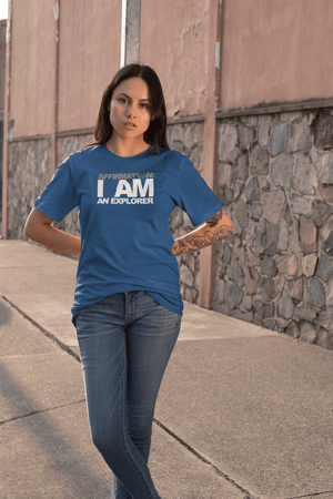 A woman wearing a blue t - shirt with the affirmation "I AM AN EXPLORER" from Boss Uncaged Store and jeans.