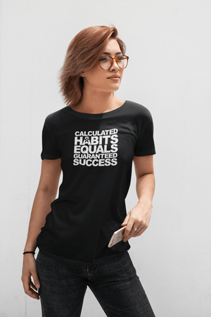 A woman wearing glasses and a black t-shirt that reads, 'CALCULATED HABITS EQUALS GUARANTEED SUCCESS.' (Buteke).
