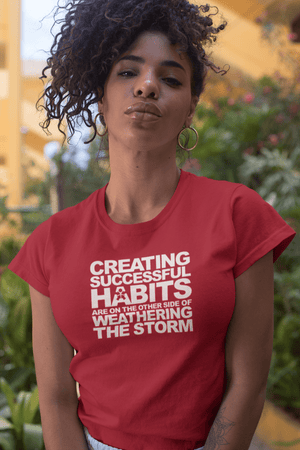 A woman wearing a red t-shirt that says "CREATING SUCCESSFUL HABITS ARE ON THE OTHER SIDE OF WEATHERING THE STORM" from Boss Uncaged Store.